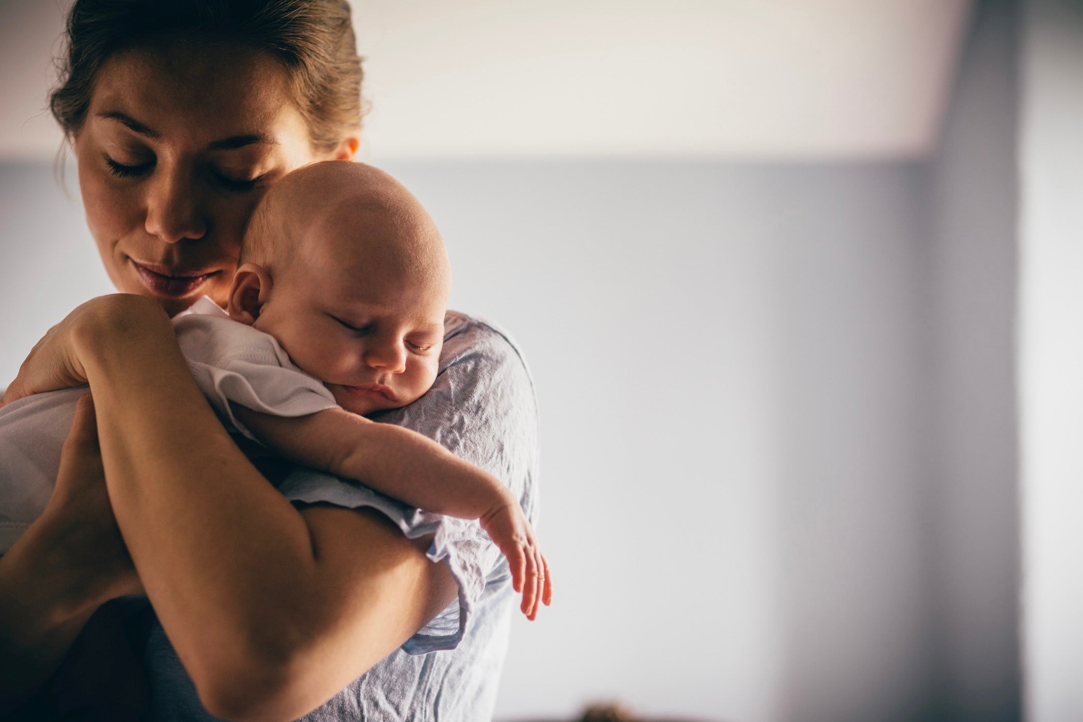 Mother lovingly holding her sleeping baby on her shoulder, gently leaning her head against the infant in a tender embrace — symbolizing comfort, safety, and the bond of baby care.