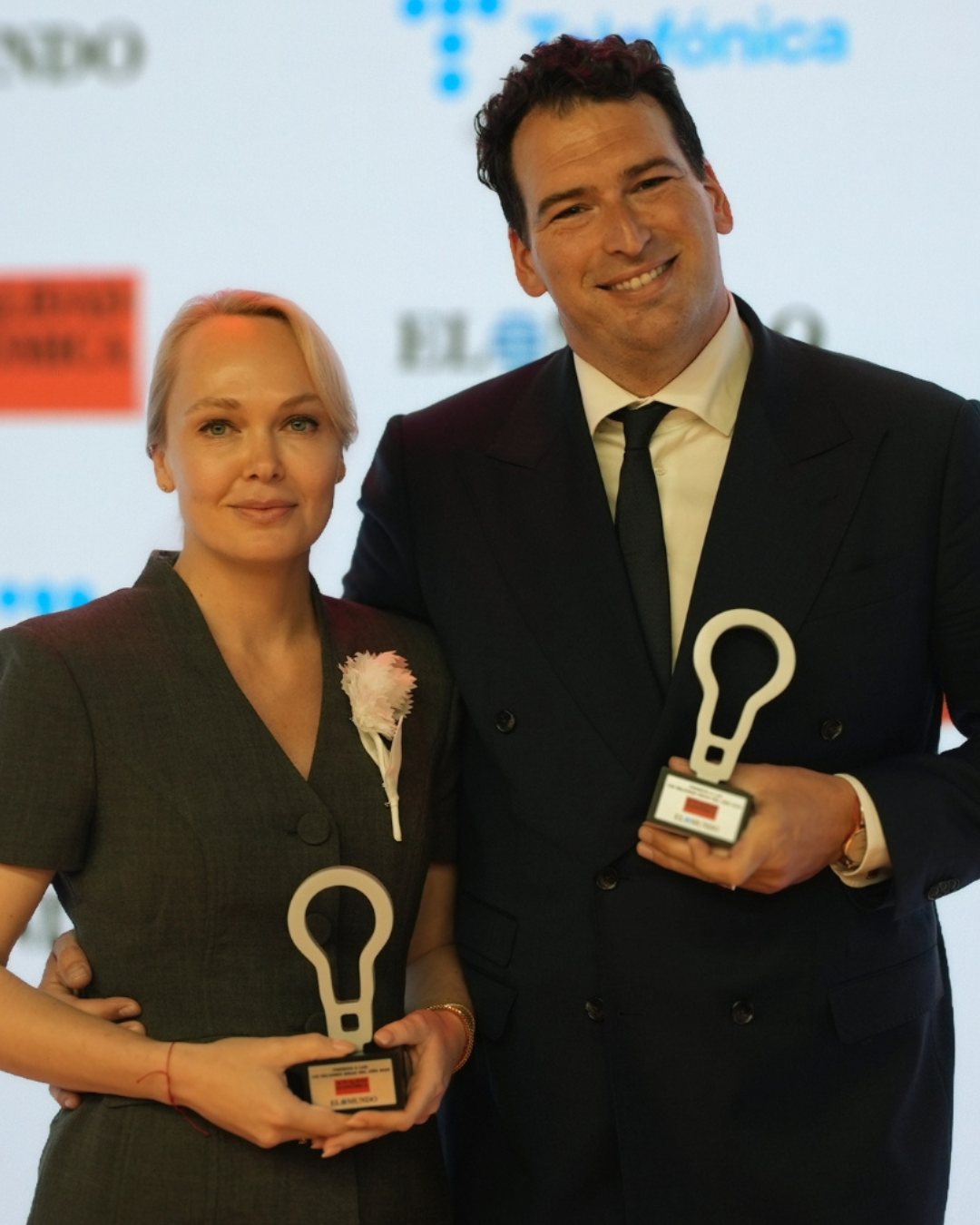 Kristina Lileeva, fundadora y CEO de Cybele Star, posa con el galardón de los premios Las 100 Mejores Ideas de 2026. Al fondo aparece la pantalla oficial del evento con los logos de Actualidad Económica, El Mundo y Telefónica.